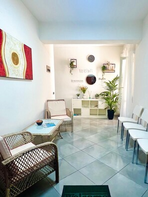 A reception area with wicker furniture, a white console table, potted plants, and a welcome sign. - Elios Rooms Tro (Tropea)