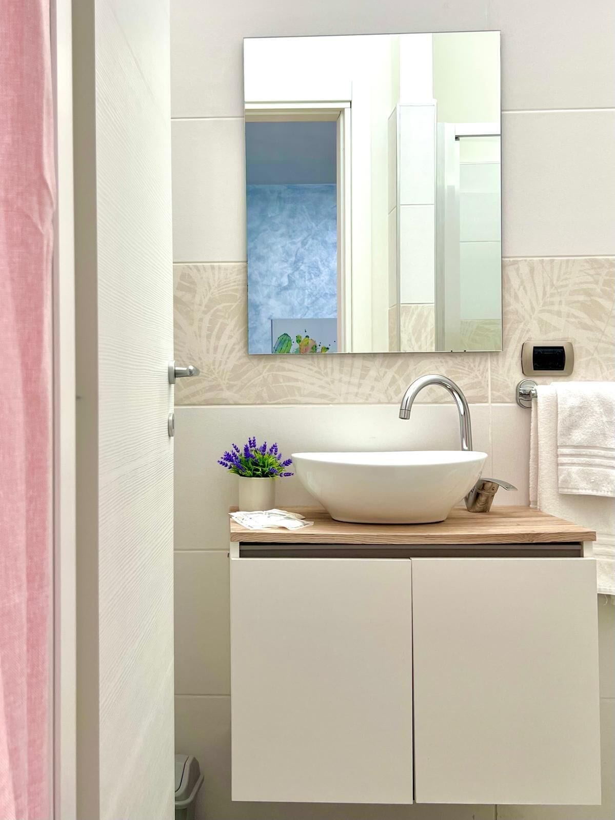 A modern bathroom with a white sink, a mirror, and a small potted plant.