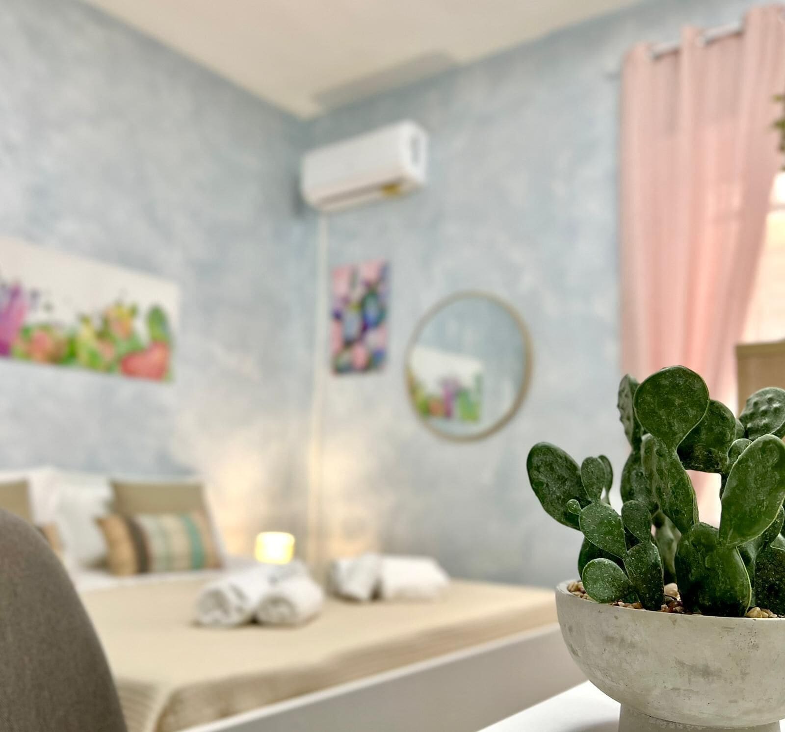 Un dormitorio con cama, un cactus en maceta, aire acondicionado de pared y un cuadro.