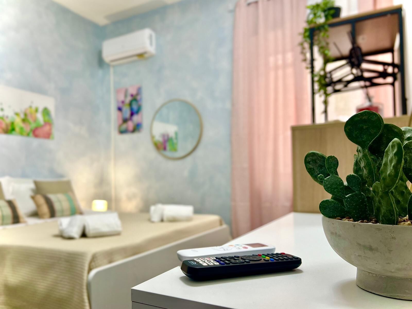 A hotel room with a bed, a remote control, a potted plant, and a wall-mounted air conditioner.