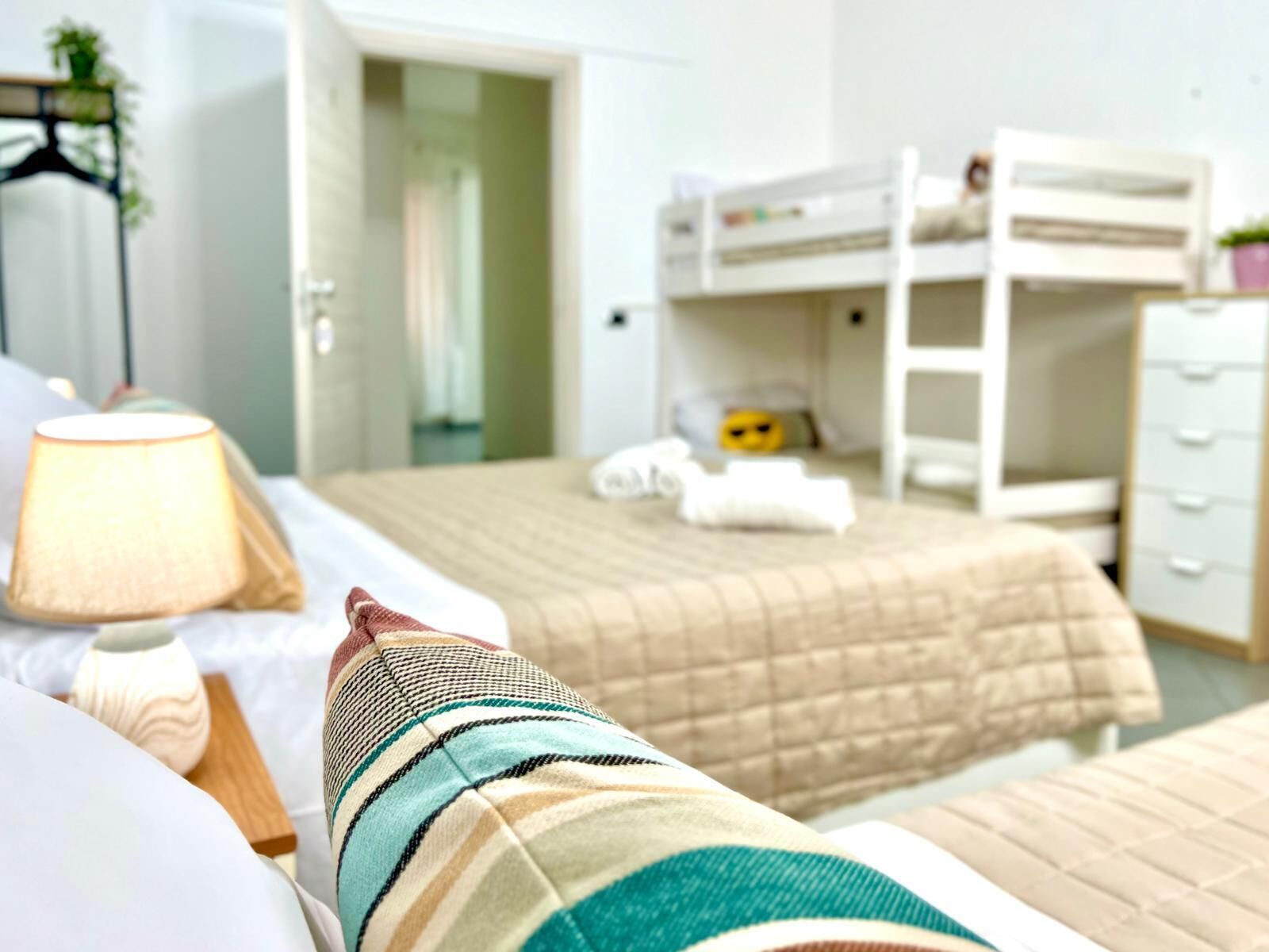 A bedroom with a bunk bed, a bedside table with a lamp, a striped pillow, and a dresser.