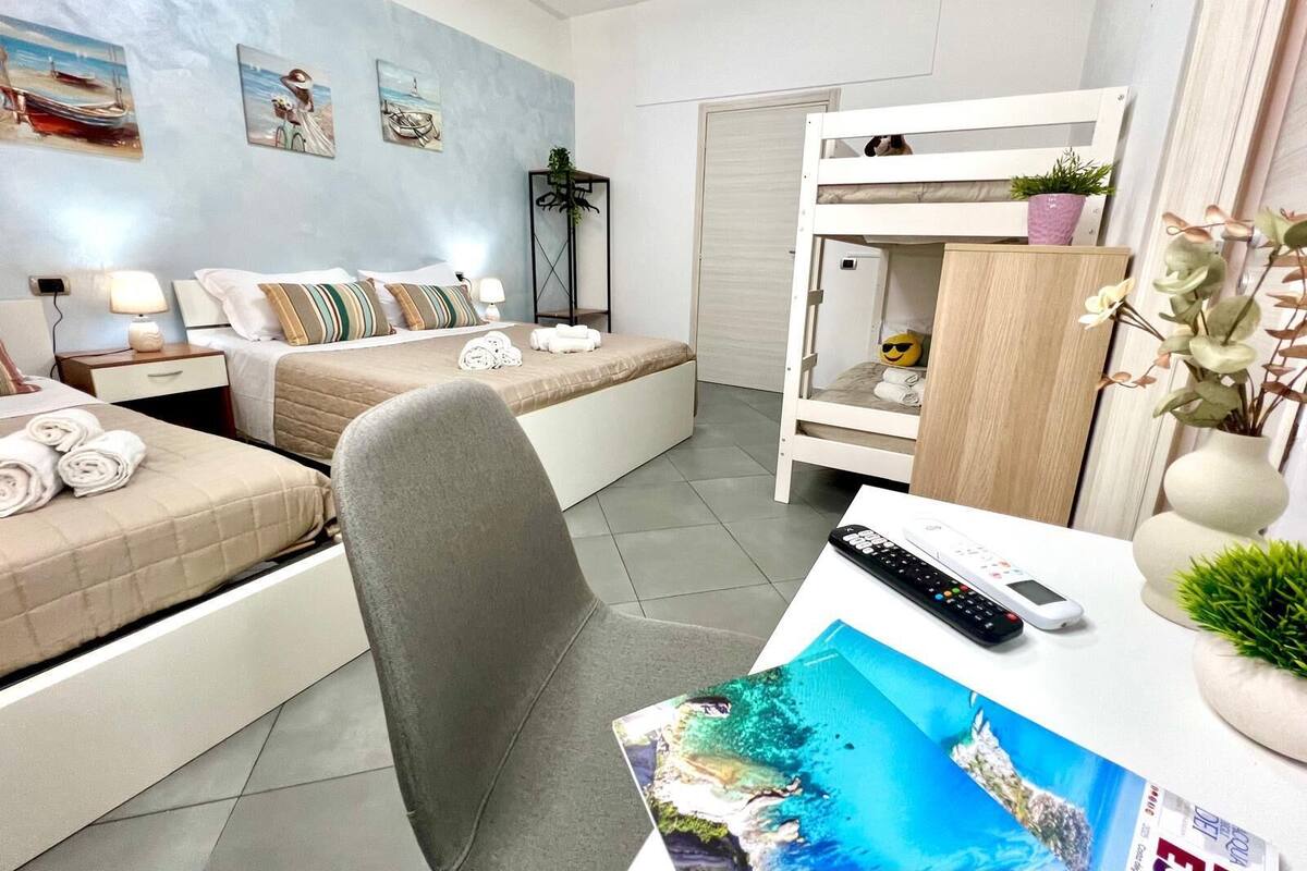 A hotel room with a bed, a desk with a remote control, a chair, and a bunk bed.