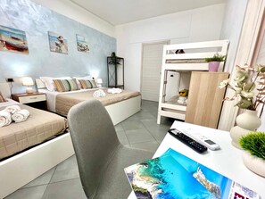 A hotel room with a bed, a desk with a remote control, a chair, and a bunk bed. - Elios Rooms Tro (Tropea)