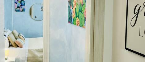 A hotel room with a bed, a bedside table, a wall-mounted mirror, and a painting of cacti.