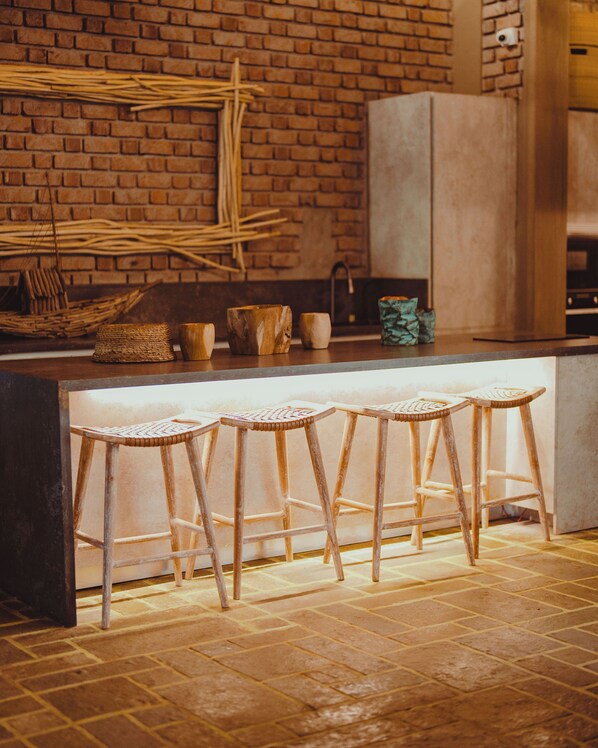 A kitchen with a brick wall, a wooden counter, and four woven stools.