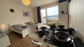 Moderni hotellihuone, jossa on sänky, mustilla astioilla katettu ruokapöytä, ruukkukasvi ja näkymä ulos.