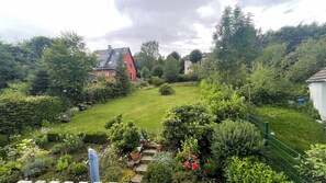 Um jardim com gramado, plantas em vasos e um edifício vermelho.