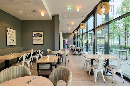 A restaurant with indoor seating, large windows, and artwork on the walls.. Premier Inn München City West