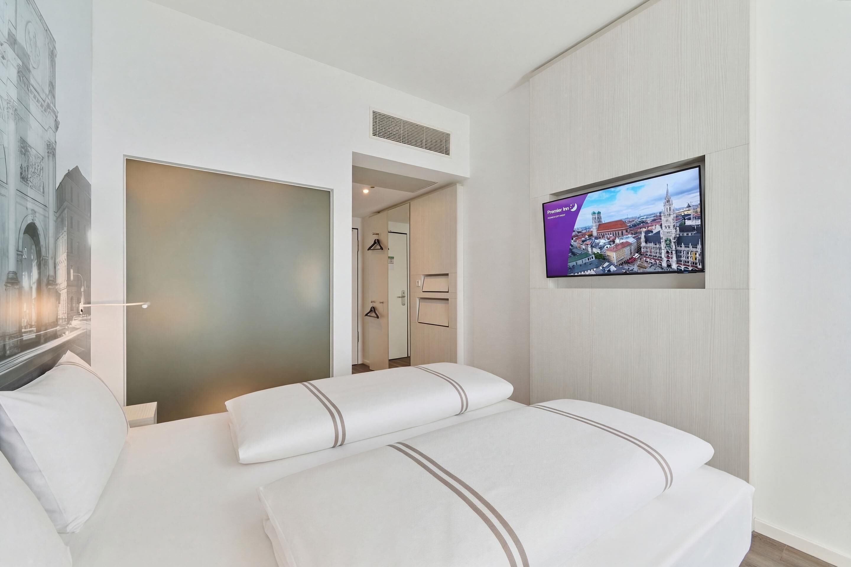 A hotel room with a bed, a television, and a view of a cityscape.