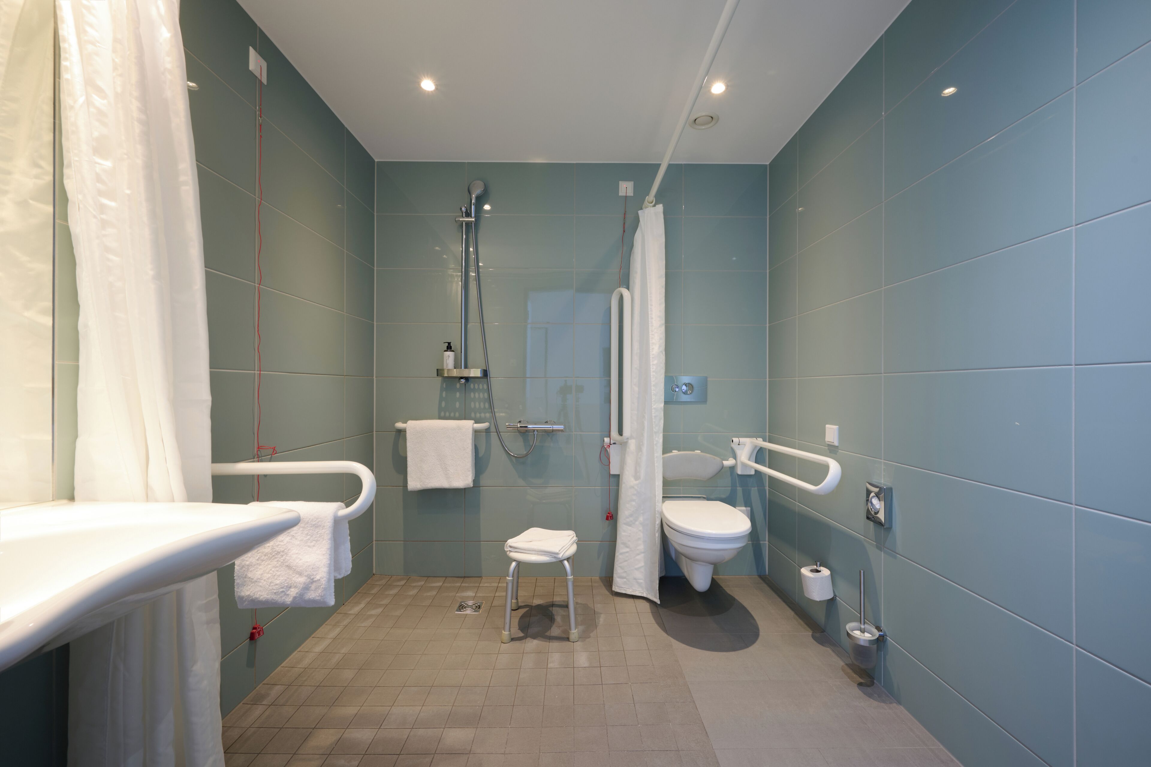 A bathroom with a shower, toilet, and a small stool.