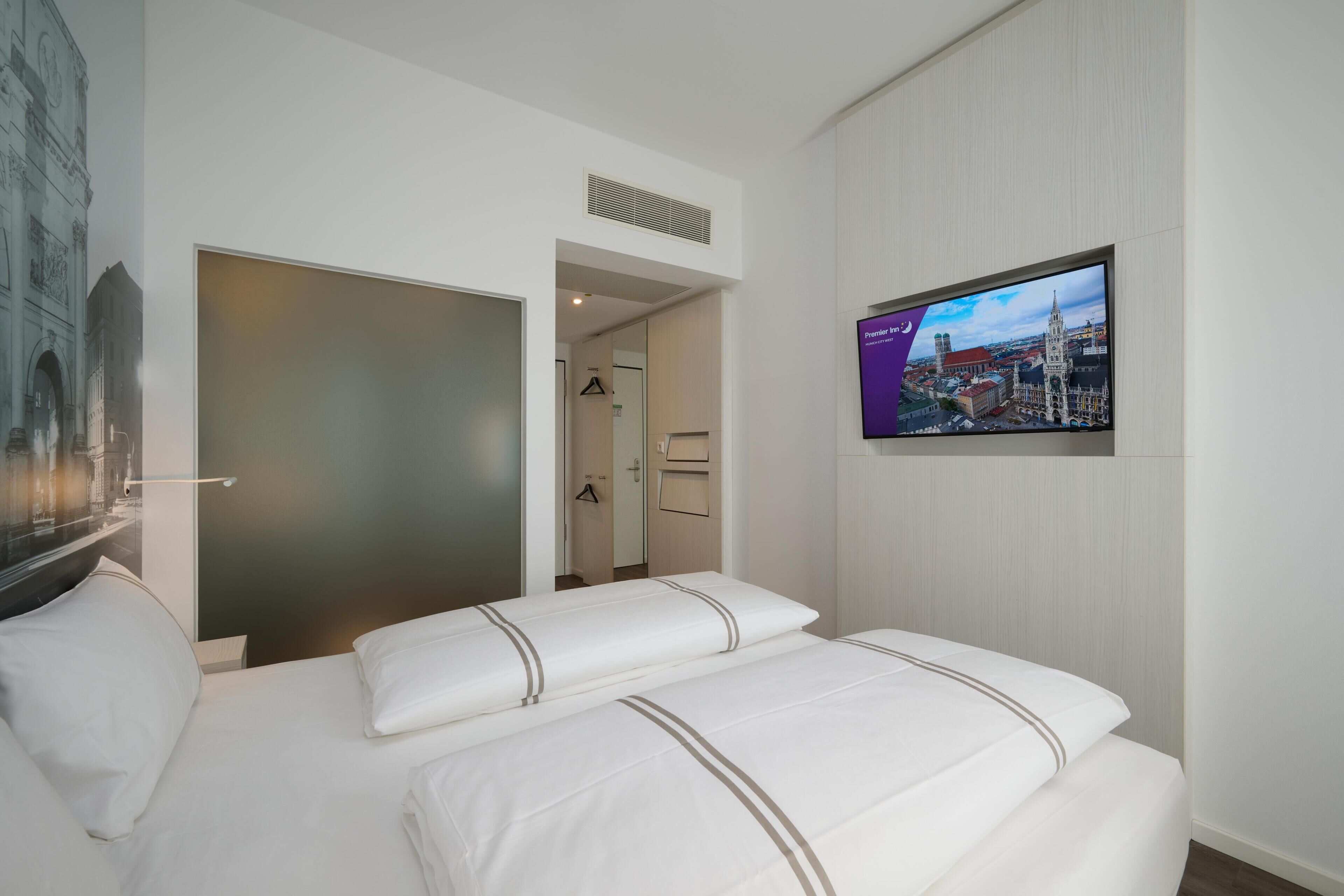 A hotel room with a bed, a television mounted on the wall, and a door leading to a hallway.