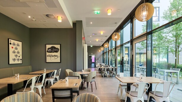 A restaurant with indoor seating, large windows, and artwork on the walls. - Premier Inn München City West (Munich)