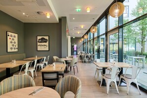 A restaurant with indoor seating, large windows, and artwork on the walls. - Premier Inn München City West (Munich)