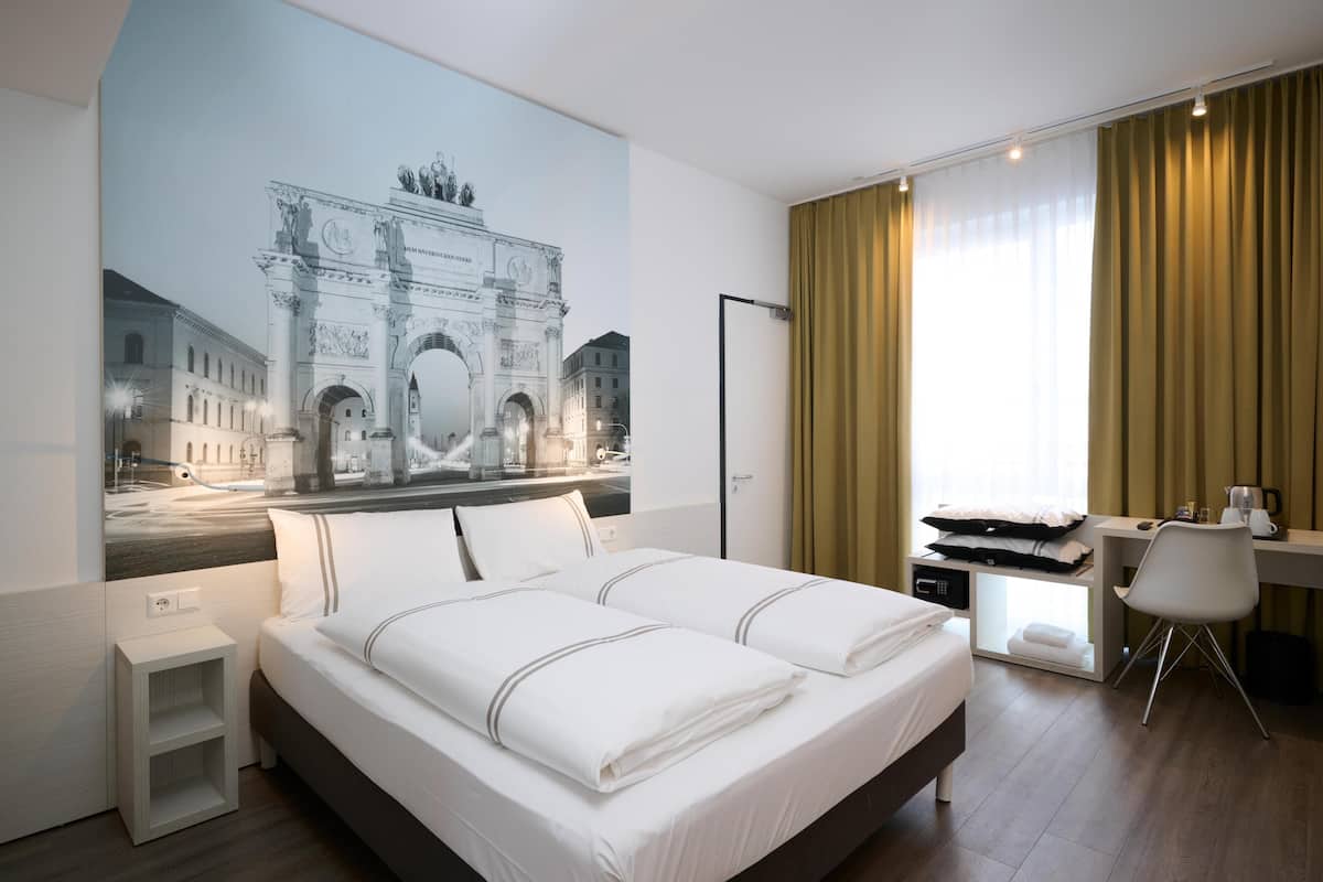 Ein Hotelzimmer mit einem großen Bett, einem Schreibtisch, einem Stuhl, einem kleinen Nachttisch und einem flachbildfernseher an der Wand.