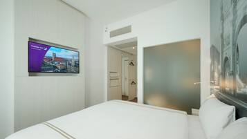 Una habitación de hotel con una cama, un televisor mostrando el logotipo de Premier Inn, una puerta que da a un baño y una obra de arte colgada en la pared.