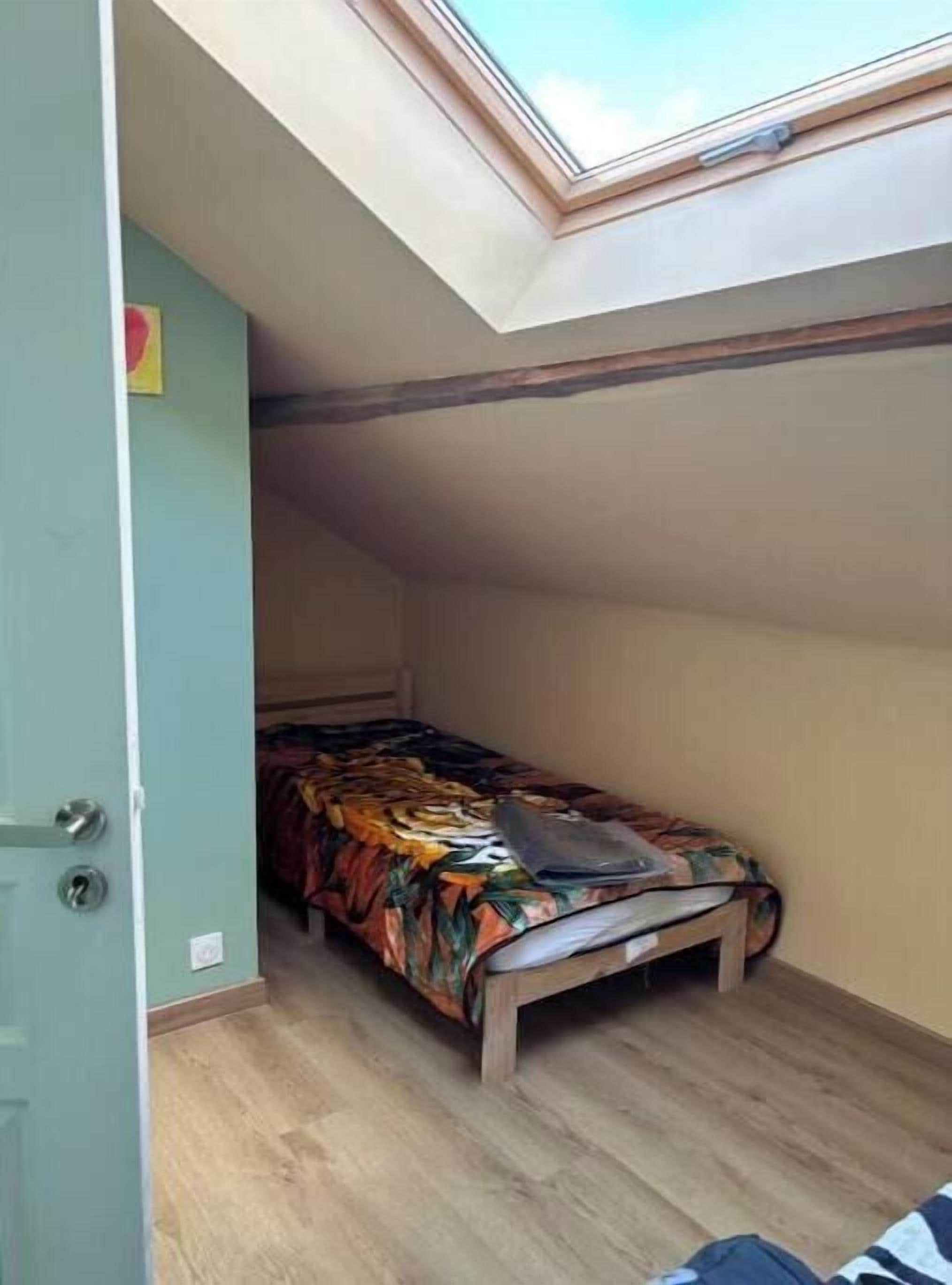 A small room with a single bed, a skylight, and a door.