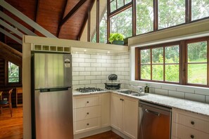 Una cocina con gabinetes blancos, un refrigerador de acero inoxidable, una estufa y una ventana con vistas al verdor.