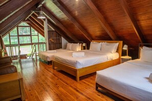 Una habitación espaciosa con techos altos y vigas de madera, dos camas con sábanas blancas, un banco de madera y un ventanal grande.