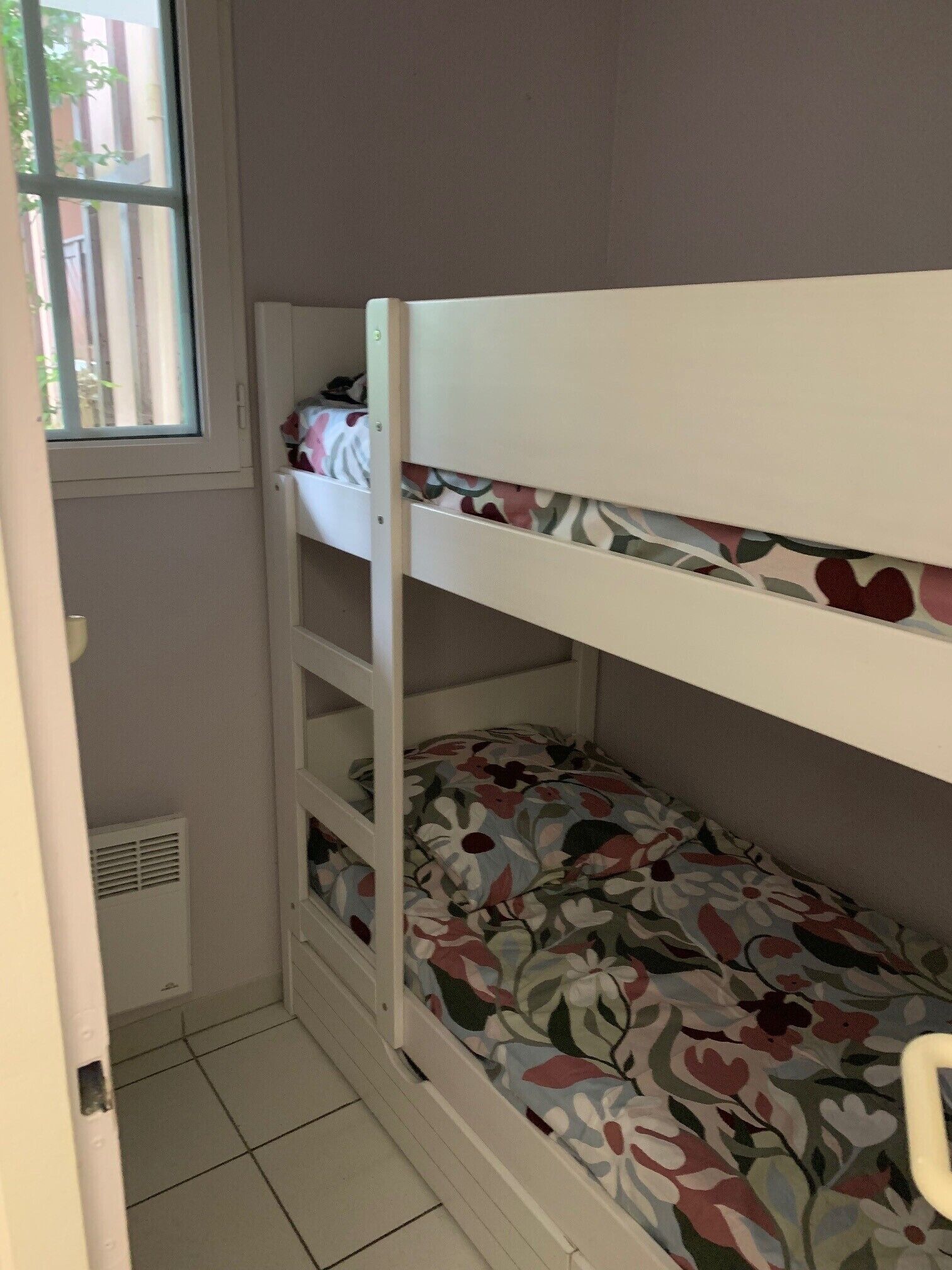 Een stapelbed met bloemenbeddengoed, een raam en een ventilatieopening.