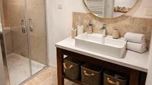 A bathroom with a glass shower enclosure, a white sink with a round mirror, and a wooden vanity with storage drawers.