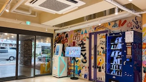 A hotel entrance with a glass door, a vending machine, and a colorful mural on the wall.