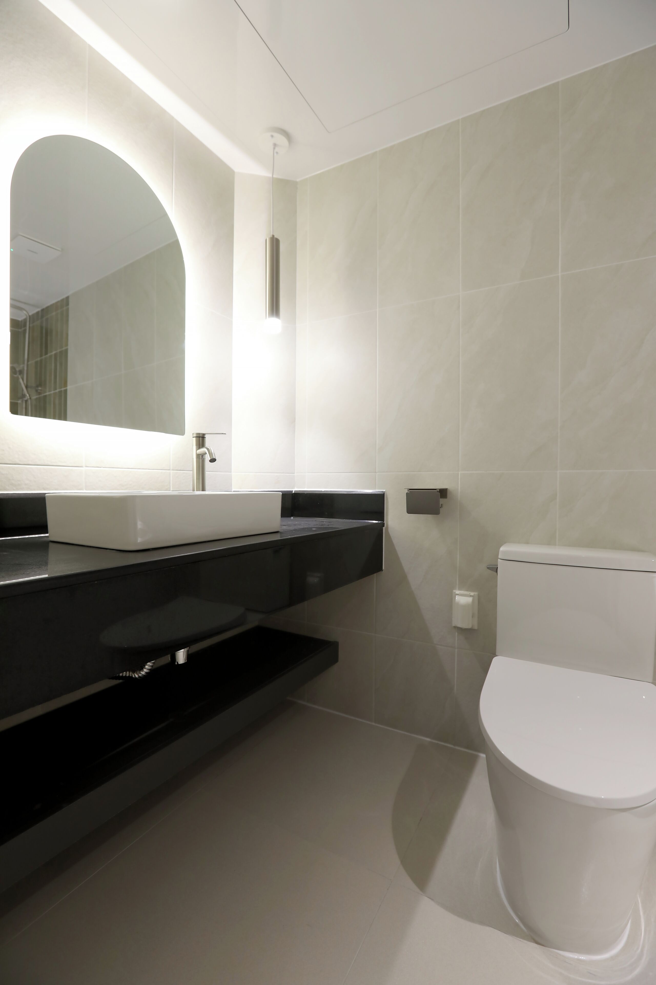 Un baño moderno con un lavamanos blanco, encimera negra y un inodoro blanco.