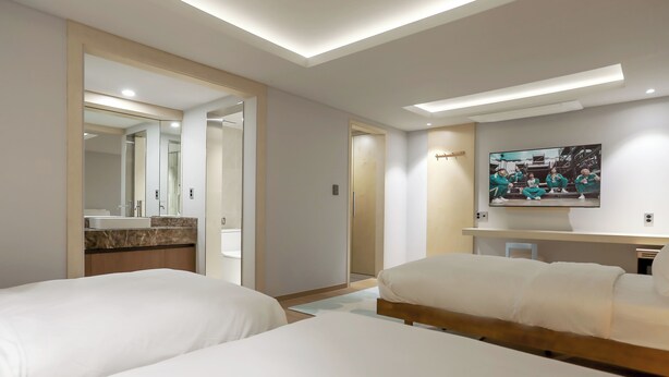 A hotel room with two beds, a bathroom with a mirror and sink, and a TV on the wall.