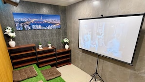 A conference room with a large screen, a cityscape painting, wooden shelves, and green artificial grass.