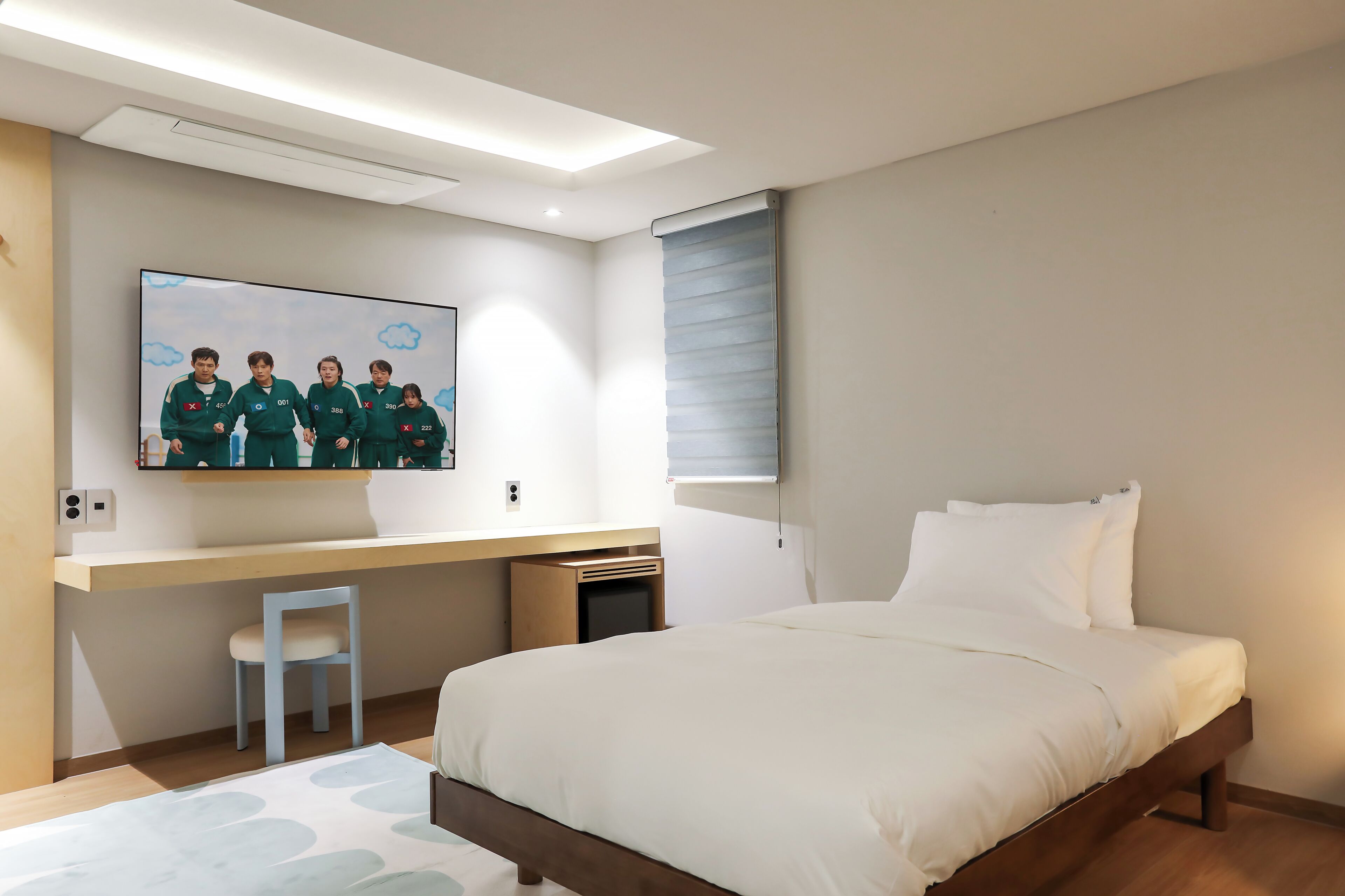 Une chambre à coucher moderne avec un lit, un bureau, une chaise, un téléviseur et une fenêtre.