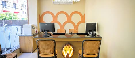 Una recepción con dos monitores de computadora, una lámpara moderna y una pared decorativa con un diseño geométrico.