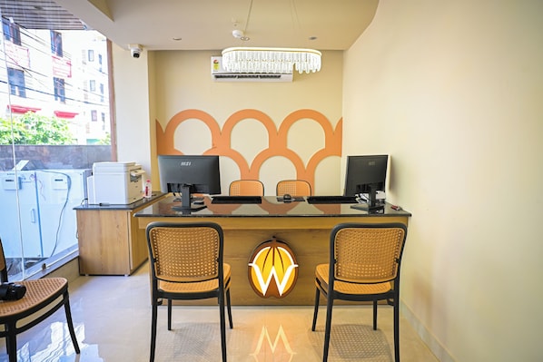 Una recepción con dos monitores de computadora, una lámpara moderna y una pared decorativa con un diseño geométrico.