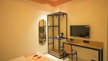 A compact room with a desk, a chair, a television, a mirror, and a wardrobe.