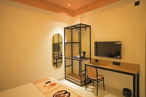 Habitación pequeña con escritorio, silla, televisor, espejo y armario.