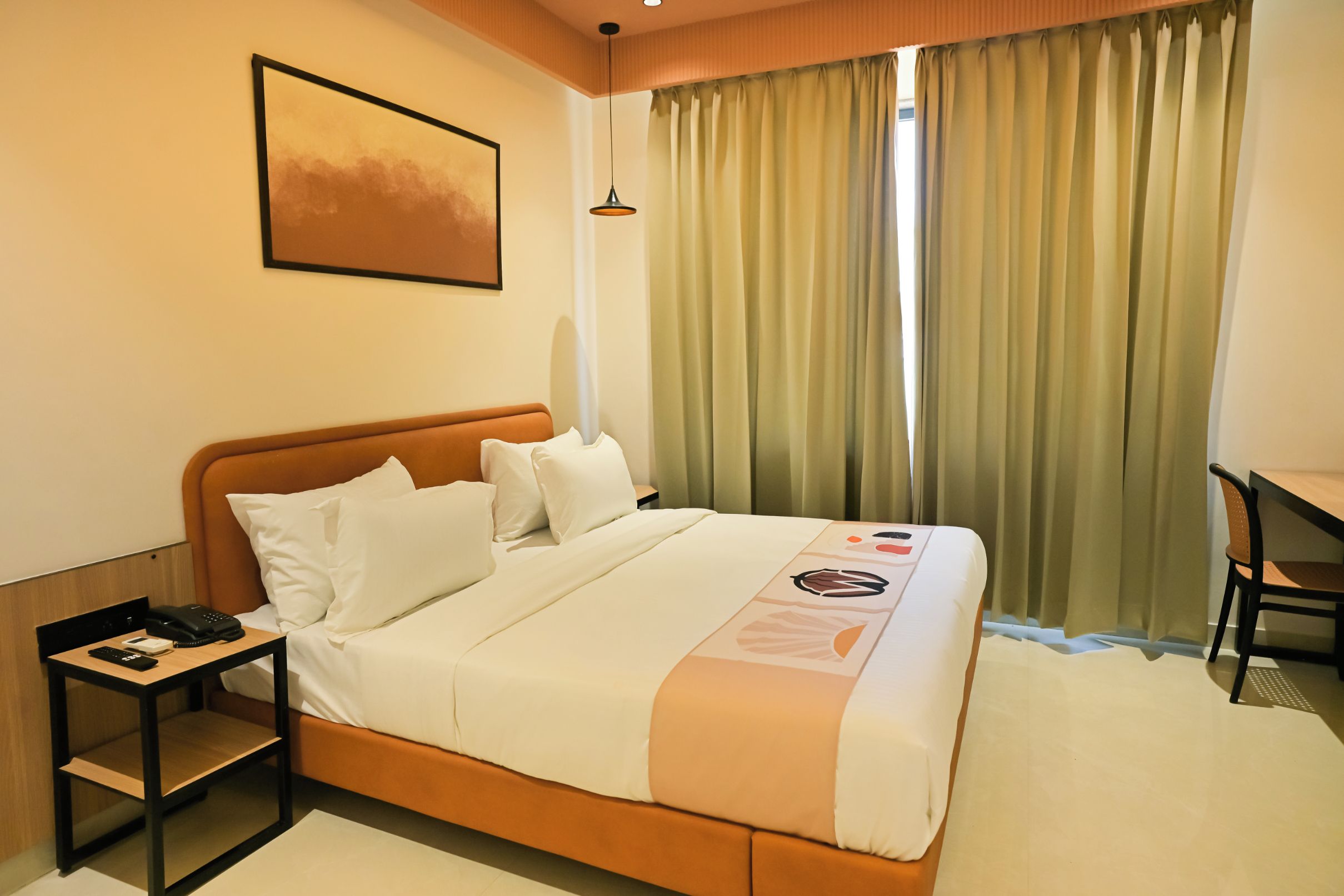 Habitación de hotel con cama, escritorio, silla, teléfono y un cuadro en la pared.