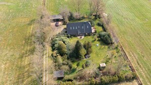 Eine Vogelperspektive zeigt ein ländliches Anwesen mit einem großen Haus, einem kleineren Gebäude und einem eingezäunten Hof mit Bäumen und einem Garten.