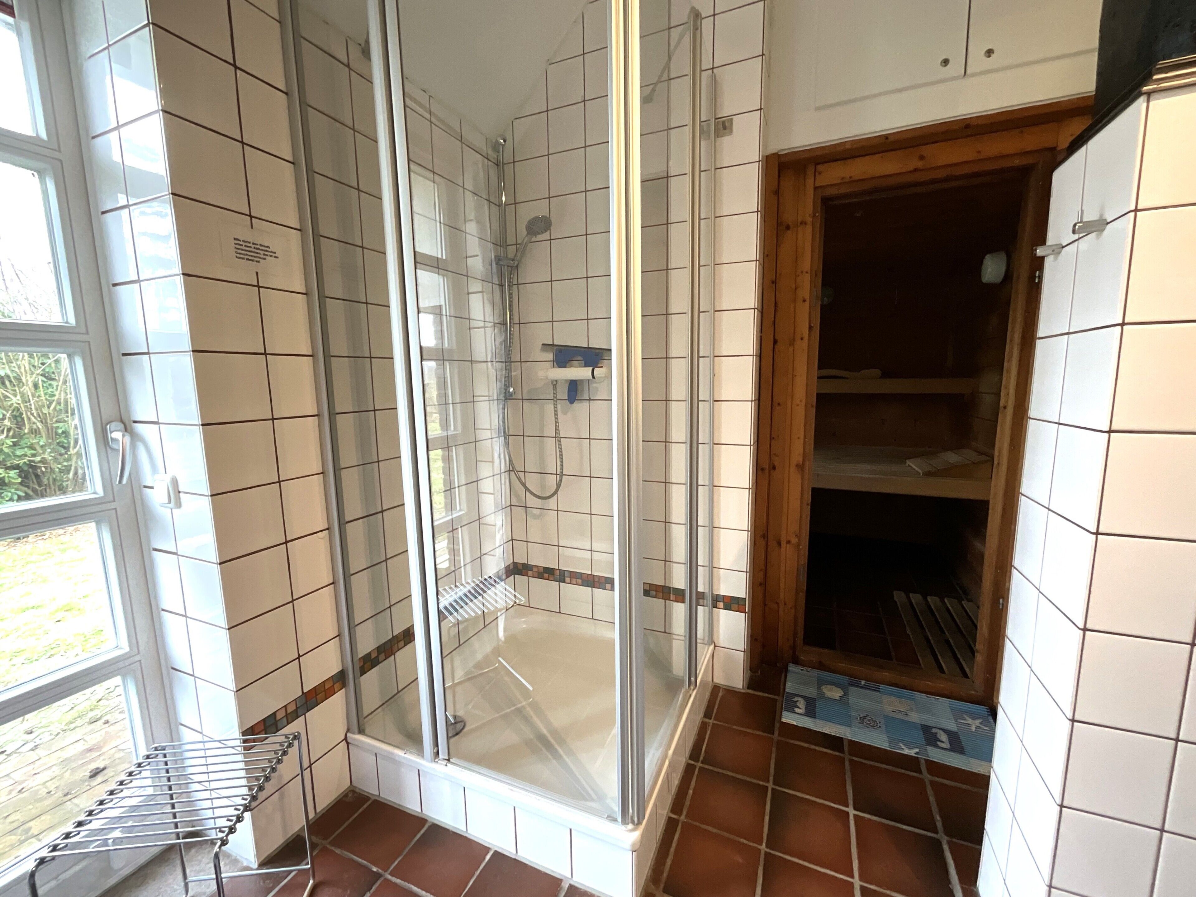 A bathroom with a glass-enclosed shower, a drying rack, and a tiled floor.