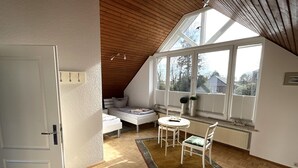 Ett sovrum med ett sluttande tak, en säng, ett litet bord och ett fönster med persienner.