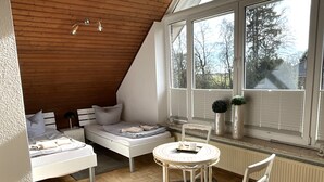 Ett sovrum med ett sluttande tak, en säng, en stol, ett bord och ett fönster med persienner.
