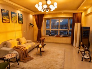 Ein Wohnzimmer mit einer Couch, einem Couchtisch, einem Fernseher und einem großen Fenster mit Vorhängen.