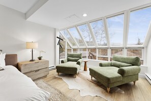 A modern bedroom with a skylight, a bed, a nightstand, a lamp, and two green armchairs. - Elegant Penthouse Connected to Grand Hyatt Vail Resort & Spa (Vail)
