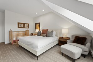 A bedroom with a large bed, a nightstand, a chair, a crib, and two wall-mounted picture frames. - Elegant Penthouse Connected to Grand Hyatt Vail Resort & Spa (Vail)