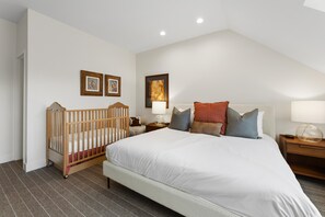 Ein Schlafzimmer mit einem großen Bett, einem Holckrippenbett, zwei Nachttischen mit Lampen und gerahmten Bildern an der Wand.