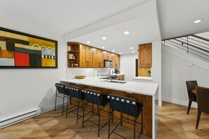 A modern kitchen with a bar area, wooden cabinets, and a large abstract painting on the wall. - Elegant Penthouse Connected to Grand Hyatt Vail Resort & Spa (Vail)