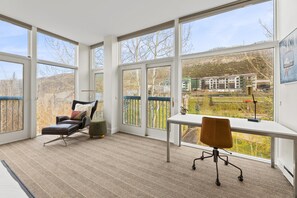 A spacious room with large windows, a leather chair, a desk, and a view of a building and trees. - Elegant Penthouse Connected to Grand Hyatt Vail Resort & Spa (Vail)