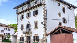 Ein zweistöckiges Gebäude mit Balkon, zahlreichen Fensterläden, einer Stein-Fassade und einem Metalldach.