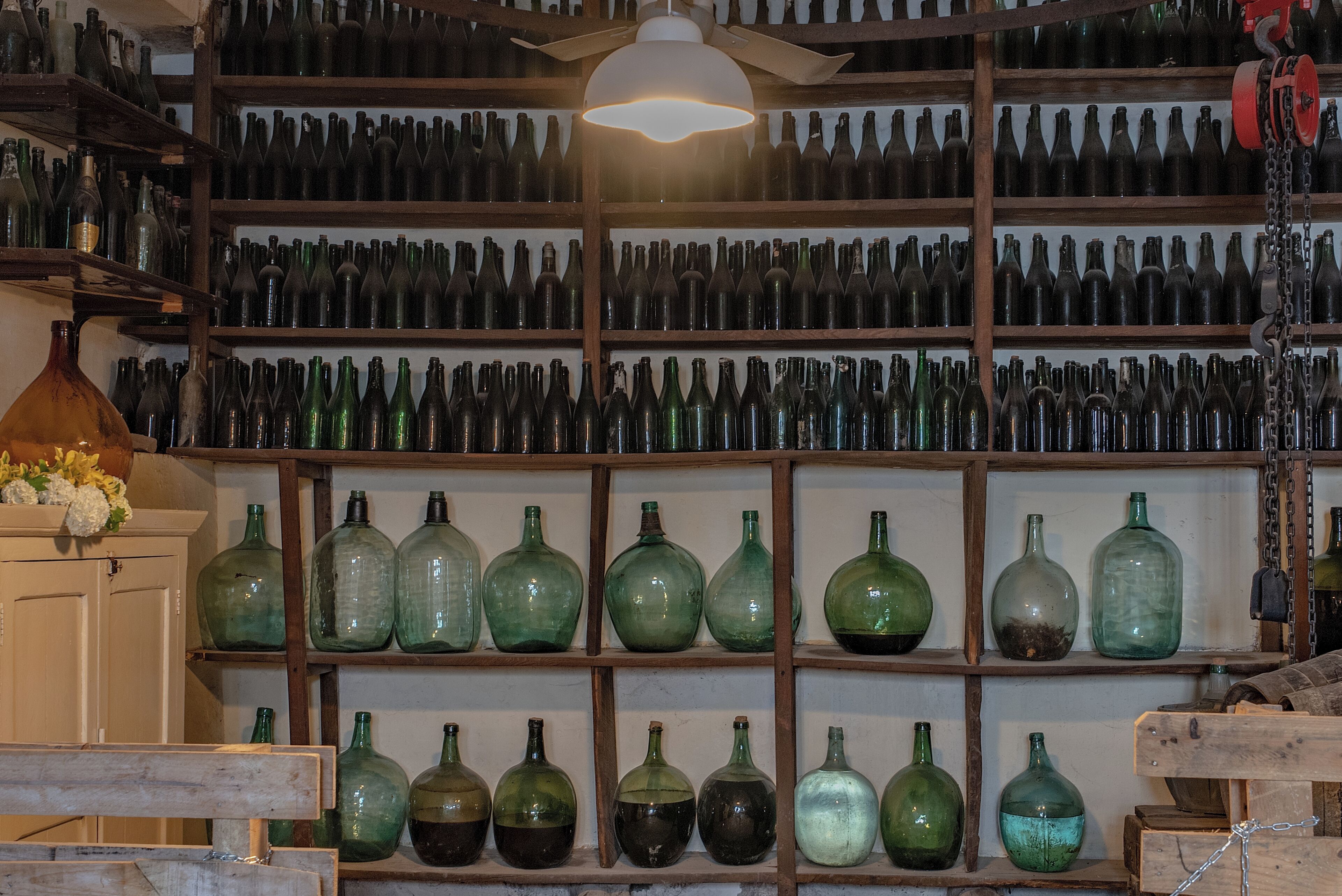 A room with shelves filled with various glass bottles, a ceiling fan, and a white door.