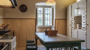 Eine Küche mit Holztisch, Hockern, einem Fenster, Schränken und einer Pendelleuchte.
