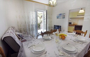 Ein Essbereich mit einem Tisch für vier Personen, eine Küche im Hintergrund und Blick ins Freie.