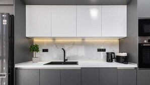 Et moderne køkken med et rustfrit stål køleskab, en sort vask, en marmor bagplade og en kaffemaskine.