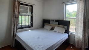 A bedroom with a bed, a ceiling fan, a window with curtains, and an air conditioning unit. - Hotel Aditya Bikaner (Bikaner)